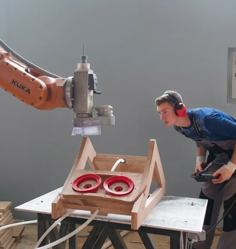 A KUKA robot arm assisting on a moulded plywood fixture in the Breza plant.