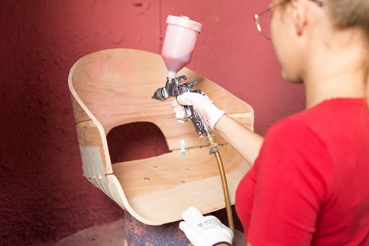 A finisher spraying a curved plywood seat shell in the finishing line.