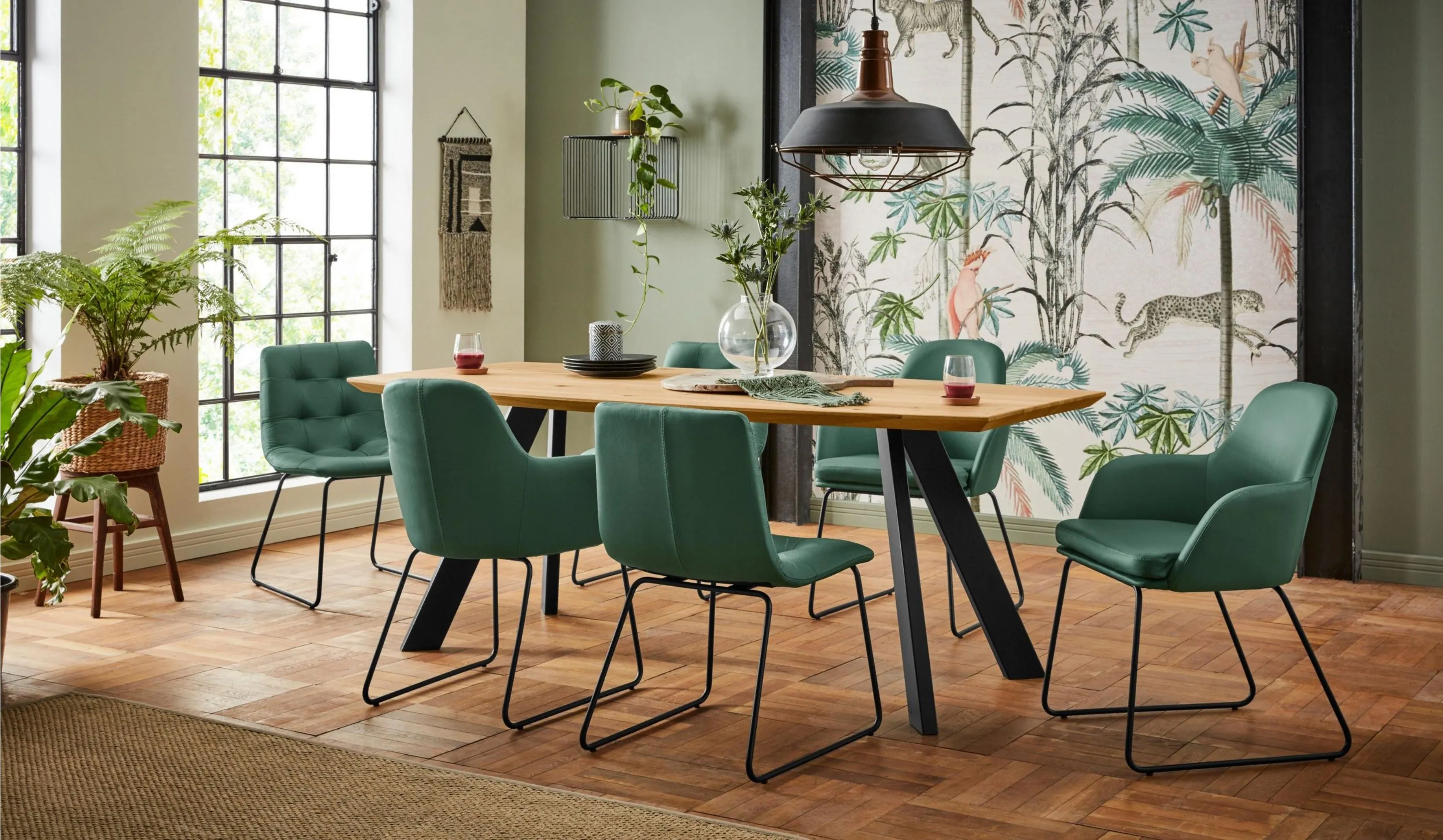 Oak top on a black metal cross base, with green velvet upholstered chairs on metal sled legs.
