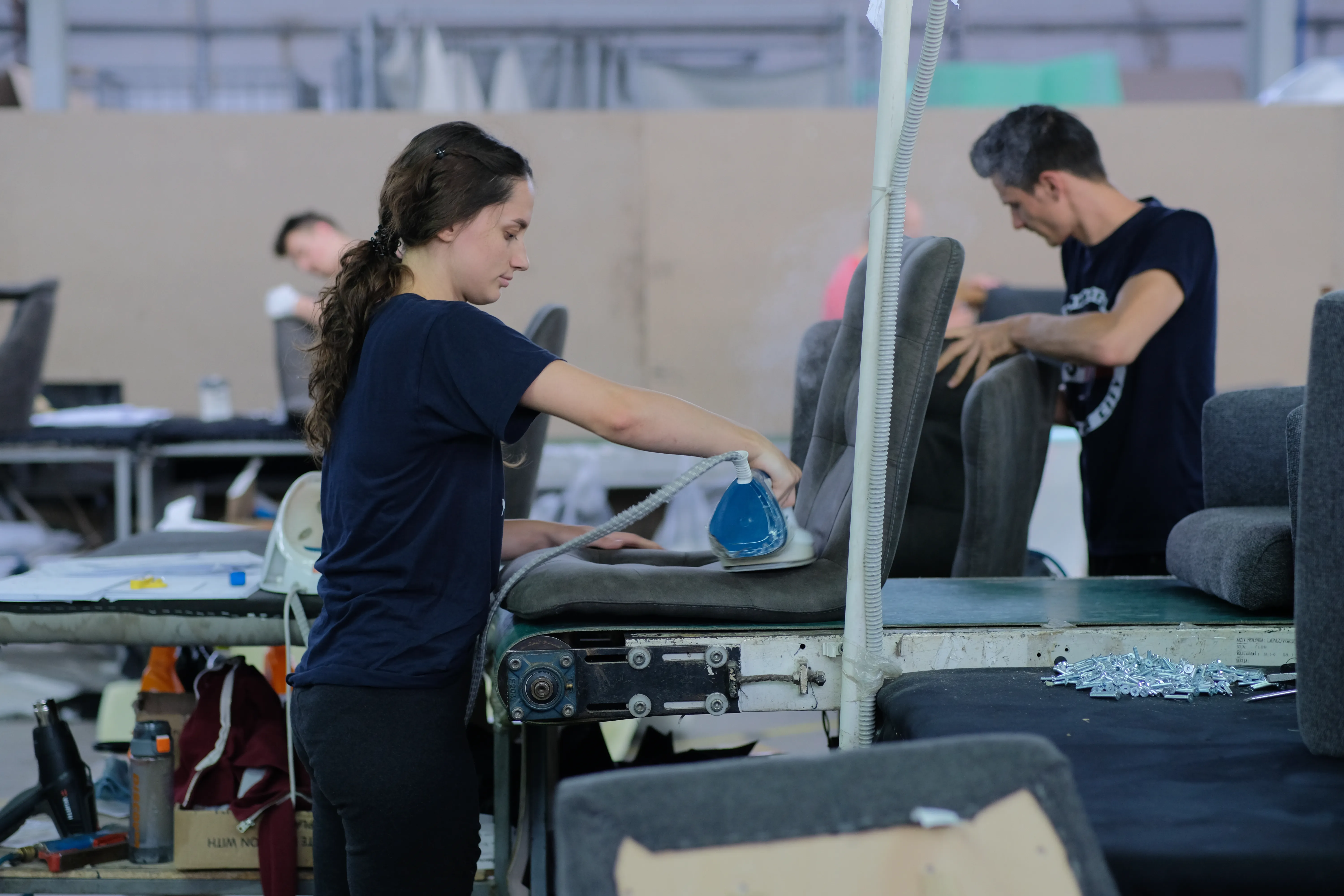 An upholsterer steaming and finishing a chair seat at the upholstery station.