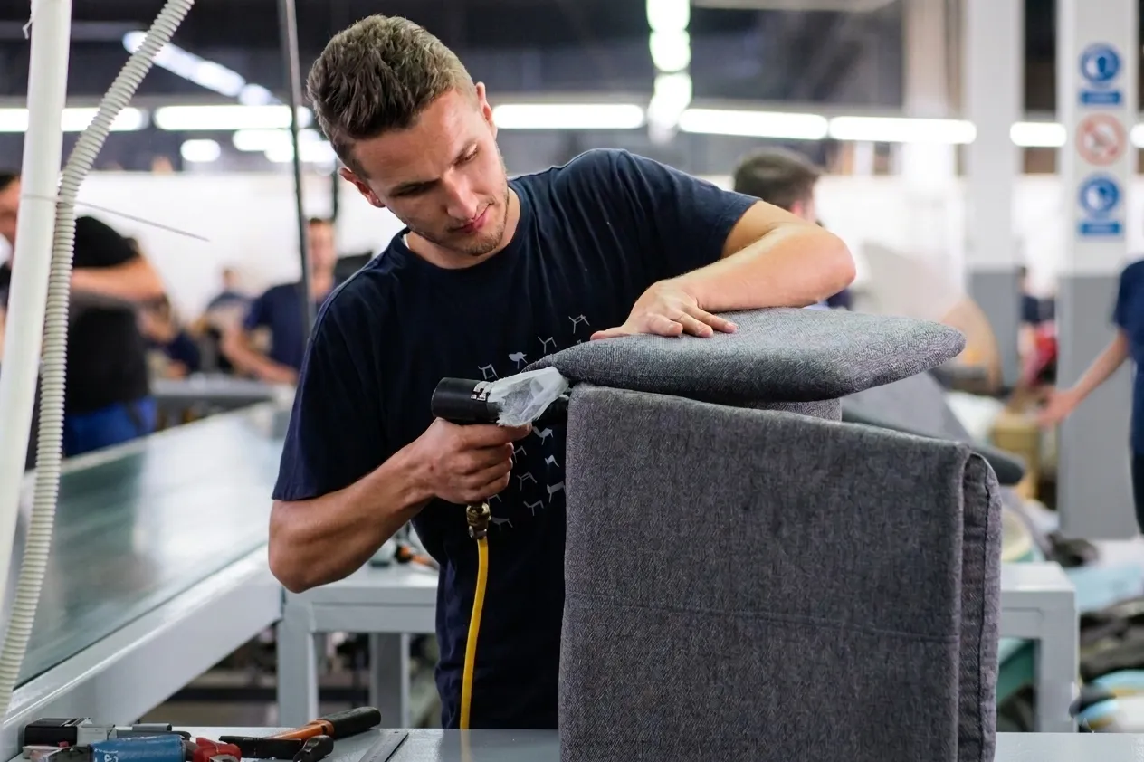 An upholsterer stretching fabric over a chair back.