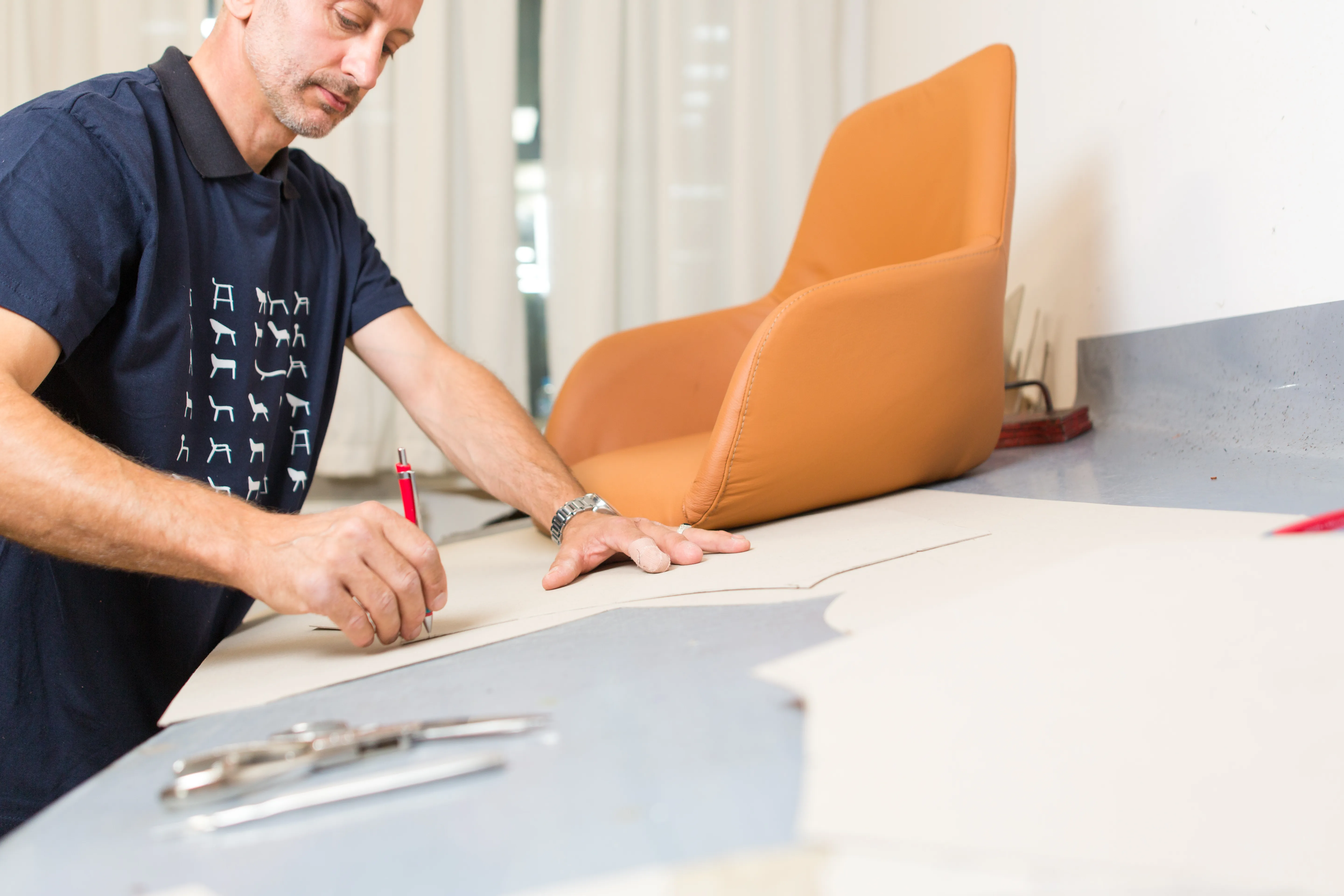 An upholsterer marking a leather panel against a finished chair.